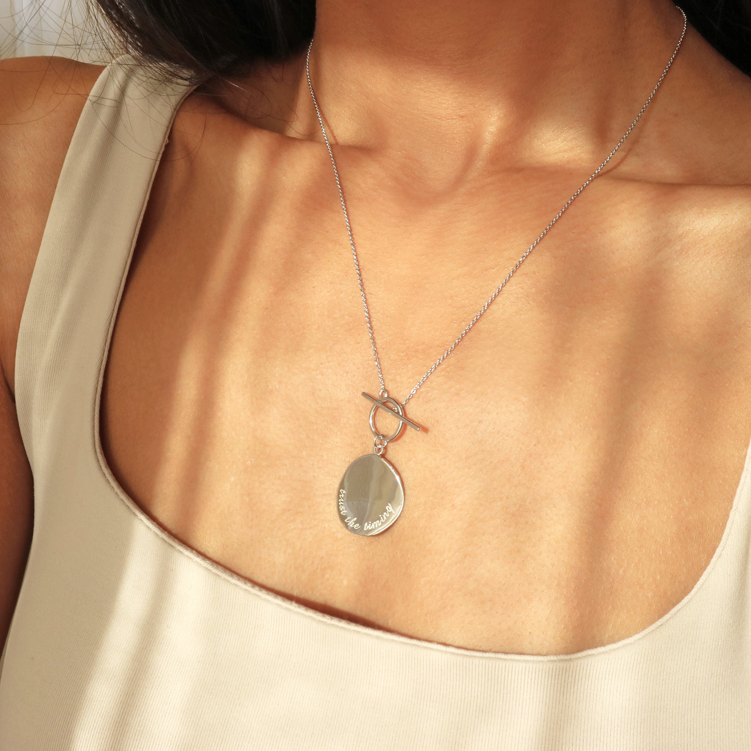 Engraved silver necklace featuring trust the timing message on a delicate disc pendant by Rani and Co