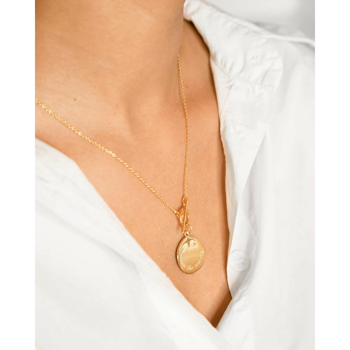"Trust the timing" engraved on a gold coin necklace with a distinctive toggle clasp.