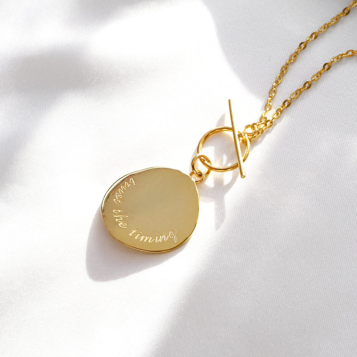 Necklace featuring a gold coin pendant with the message "trust the timing" and a secure toggle clasp, from Rani & Co.